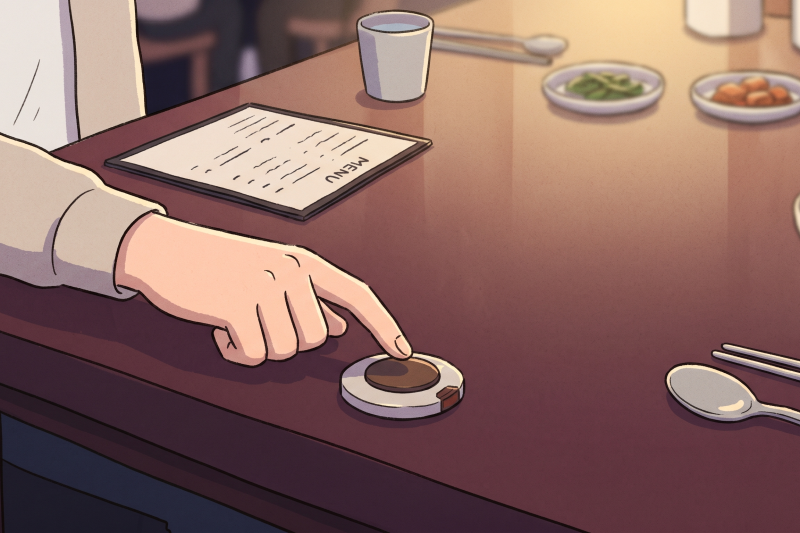 Korean restaurant call button on a dining table with a hesitant diner nearby.